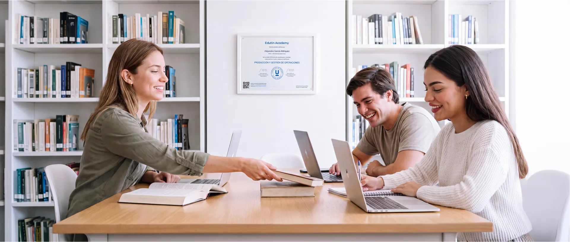 Tres estudiantes trabajando juntos en una biblioteca, con un certificado de Edutin Academy enmarcado al fondo